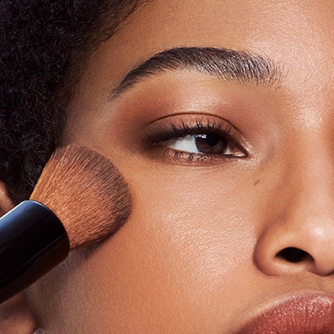 Model applying Skin Long-Wear Weightless Foundation to skin with a foundation brush